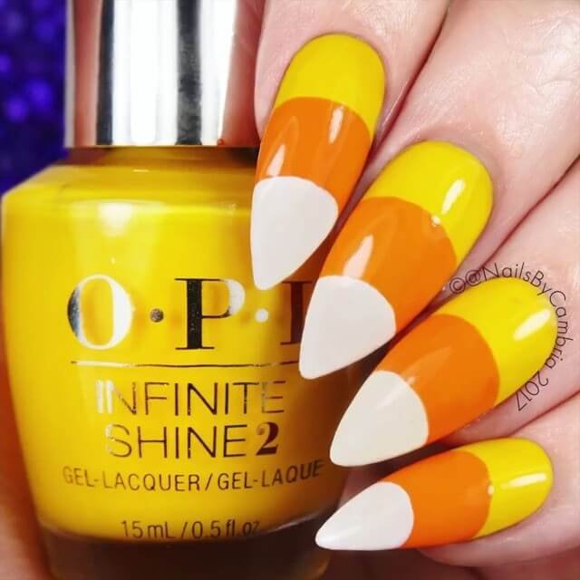 Close-up of candy corn nails with vibrant yellow, orange, and white stripes, perfect for Halloween.