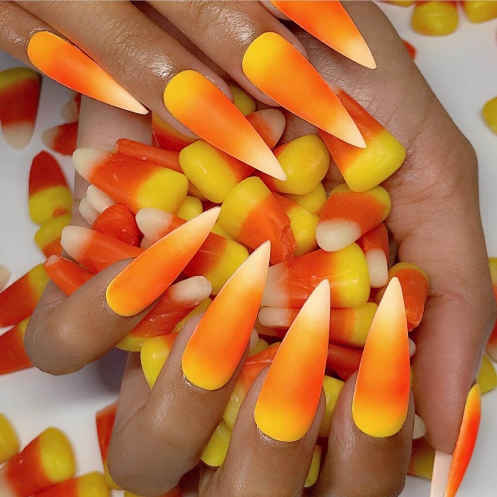 Close-up of candy corn nails with vibrant yellow, orange, and white stripes, perfect for Halloween.