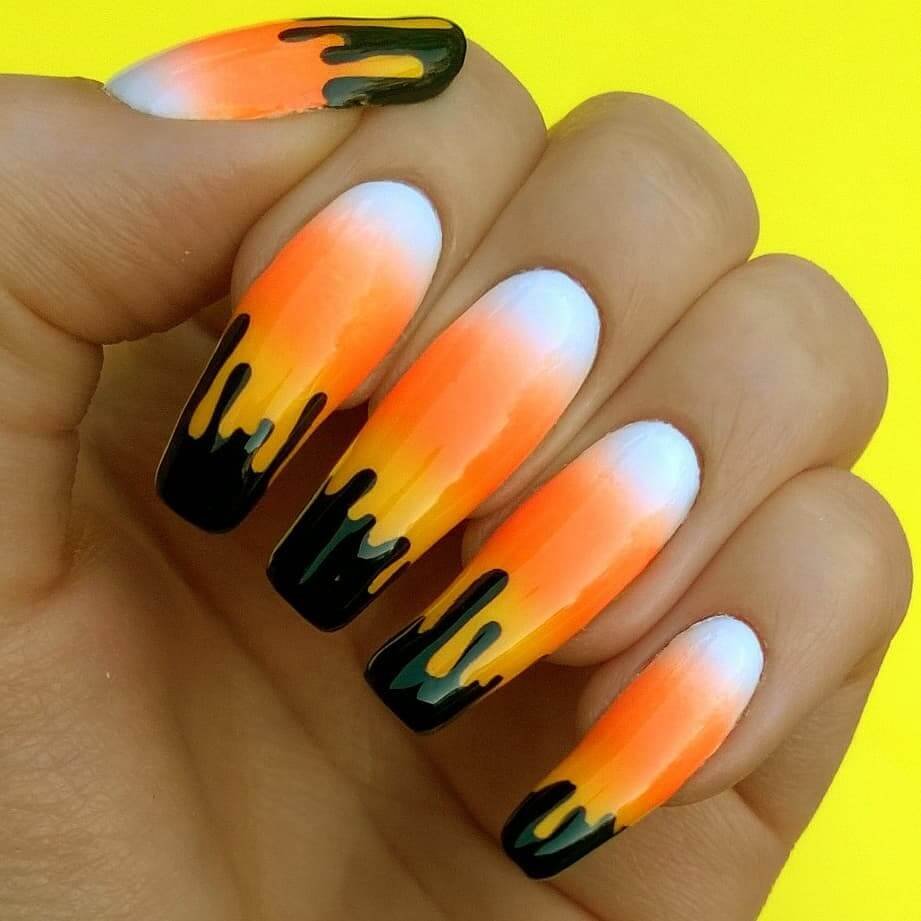 Close-up of candy corn nails with vibrant yellow, orange, and white stripes, perfect for Halloween.