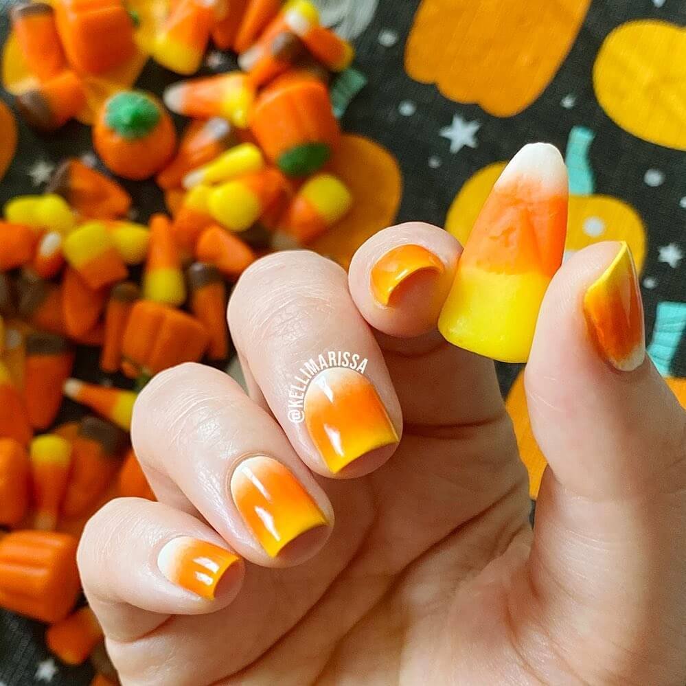 Close-up of candy corn nails with vibrant yellow, orange, and white stripes, perfect for Halloween.