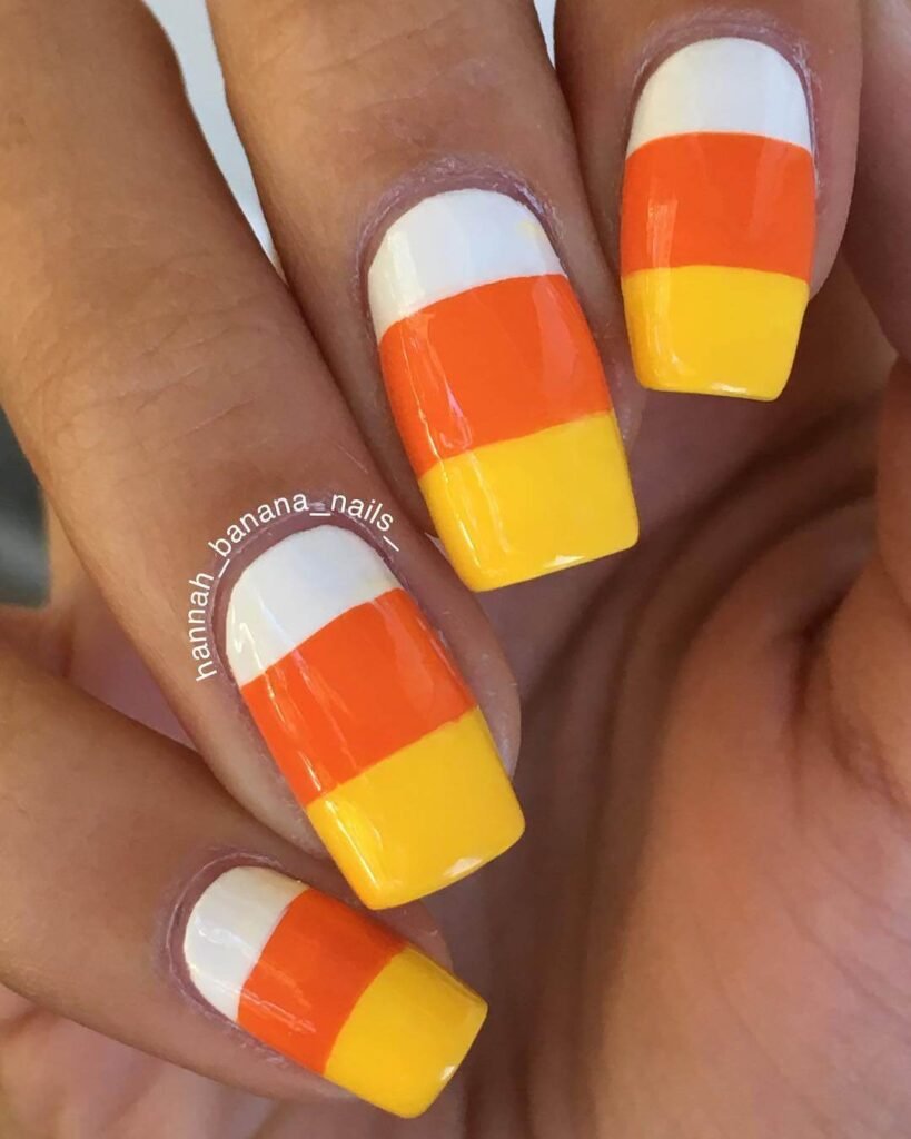 Close-up of candy corn nails with vibrant yellow, orange, and white stripes, perfect for Halloween.