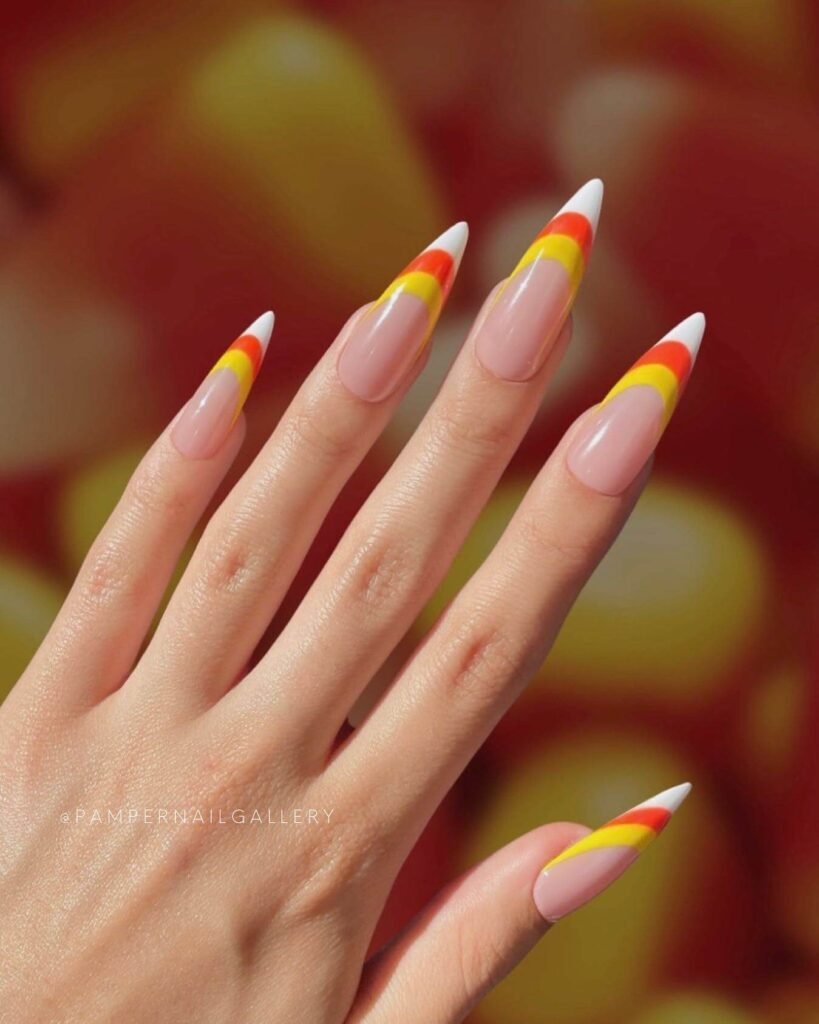 Close-up of candy corn nails with vibrant yellow, orange, and white stripes, perfect for Halloween.